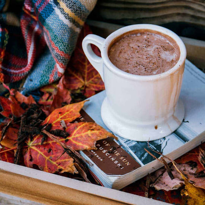 Cozy autumn scene with hot cocoa, fall leaves, book, and plaid blanket on a wooden tray