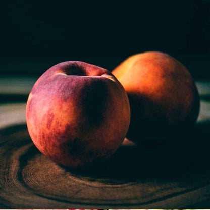 Two ripe peaches on a dark wooden board, evoking sweet fruity notes in room sprays