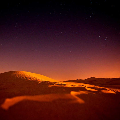 Glowing desert sand dunes under a starry night sky with deep orange and purple hues