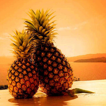 Two pineapples at sunset by the ocean, evoking tropical aroma oils