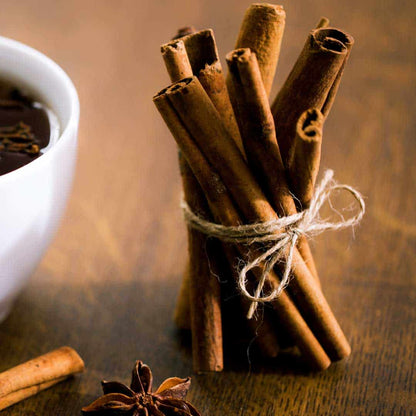 Bundle of cinnamon sticks tied with twine beside star anise and a cup of hot chocolate