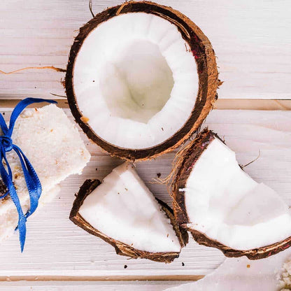 Fresh cracked coconut halves and pieces on a white wood surface, evoking natural aroma oils