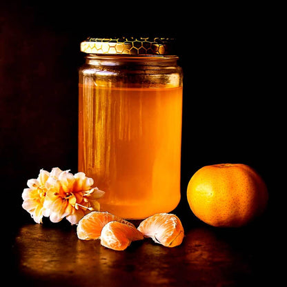 Jar of golden honey with mandarin orange segments and white flowers