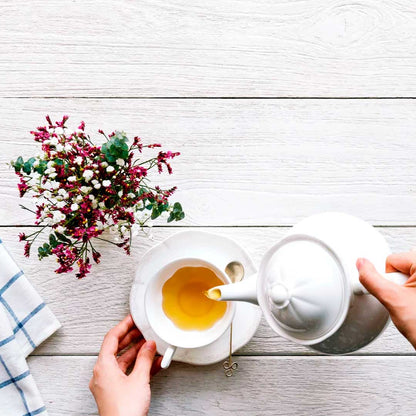 Overhead view of herbal tea being poured into a white cup with flowers