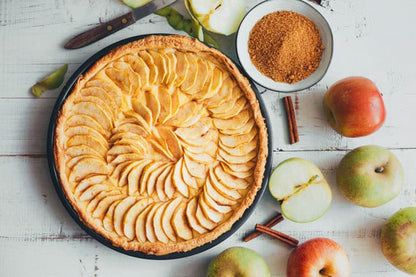 Homemade apple tart with sliced apples, cinnamon sticks, and brown sugar on white wood