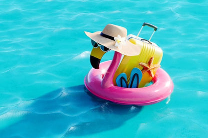 Colorful flamingo pool float with summer travel accessories in turquoise water
