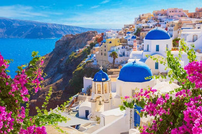 Iconic white buildings with blue domes in Santorini, Greece, framed by pink flowers