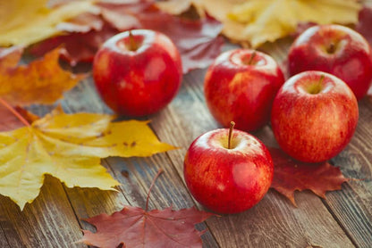 Fresh red apples and autumn maple leaves on rustic wooden surface