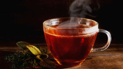 Steaming glass cup of hot black tea with fresh sage and thyme herbs on a wooden surface
