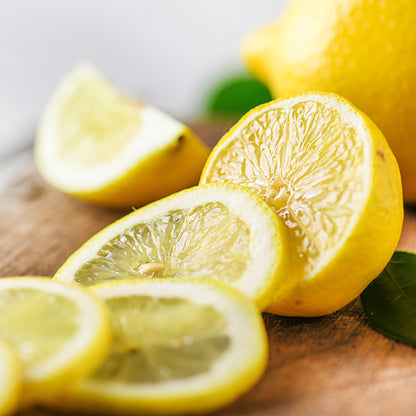 Sliced fresh lemons on a wooden cutting board with green leaves