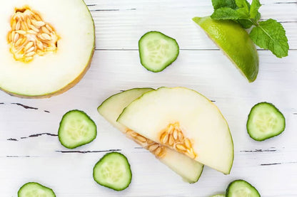 Fresh cucumber, honeydew melon, lime, and mint flat lay on white wood surface