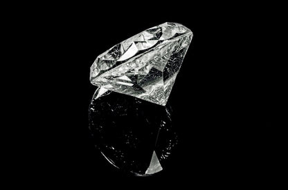 Large faceted diamond gemstone reflecting on a black surface, symbolizing luxury and premium scenting