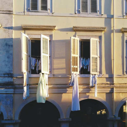European building facade with white shutters and laundry hanging from windows in warm sunlight