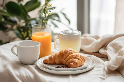 Continental breakfast in bed with croissant, orange juice, and hot tea by a bright window