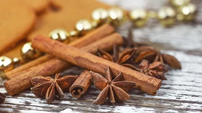 Cinnamon sticks and star anise spices on a rustic wooden surface with gold holiday beads