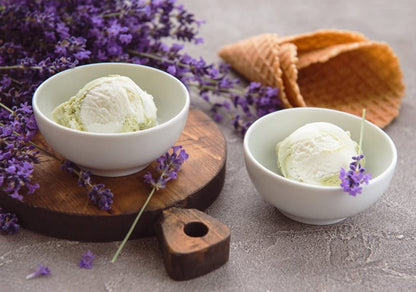 Two bowls of lavender ice cream with waffle cones and fresh purple lavender sprigs on a wooden board
