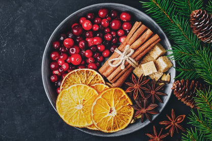 Cranberries, dried orange slices, cinnamon sticks, star anise, and brown sugar in a bowl with pine branches