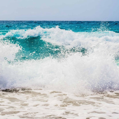 Large turquoise wave crashing onto a sandy beach with white sea foam and spray