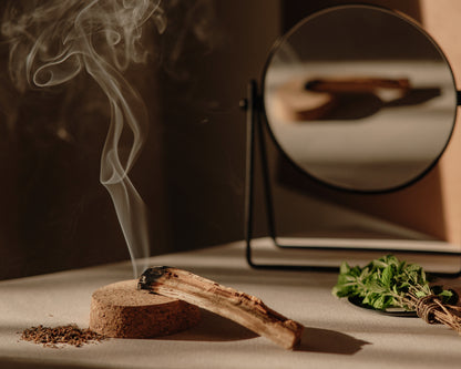 Palo santo wood smoldering on a cork stand beside fresh mint, used in spa scenting and aroma oils