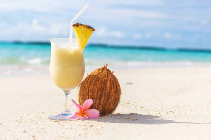 Piña colada cocktail with coconut and pineapple garnish on a tropical white sand beach