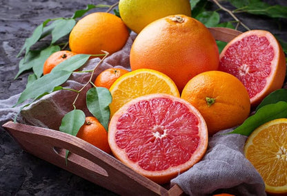 Fresh-cut grapefruits, oranges, and tangerines in a rustic wooden tray with green leaves
