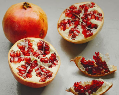 Fresh pomegranates cut open revealing vibrant red seeds on a light gray surface
