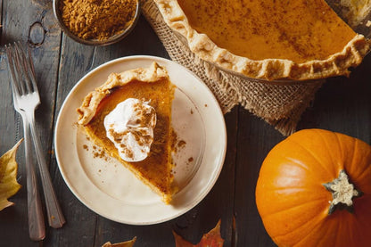 Slice of pumpkin pie topped with whipped cream beside a whole pie and pumpkins