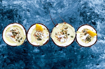 Four halved coconuts filled with creamy tropical dessert on blue textured background