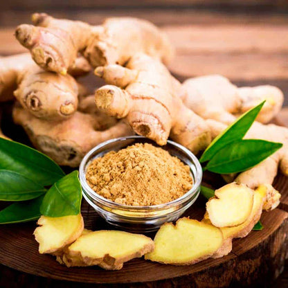 Fresh ginger root, sliced ginger, and ground ginger powder with green leaves on a wooden board